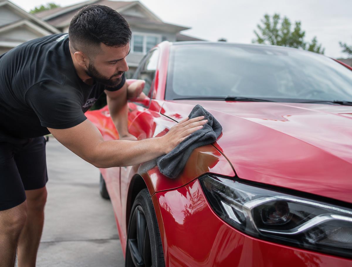 Hand-drying a red car in a driveway